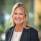 Woman with long blond hair, dark grey jacket over light top 