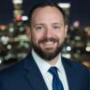 Sean in a blue suit and blue tie in front of a blurred city background