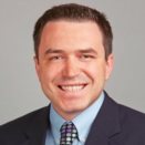 Alex Druta smiling and wearing a blue shirt, tie, and suit jacket