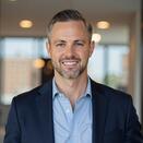 Britton Wells smiling and wearing a blue shirt with navy suit jacket