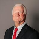 Charles de Wetter smiling and wearing a white shirt, red tie, and black suit jacket
