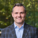 Clayton Ellis smiling and wearing a light blue shirt and plaid sport coat