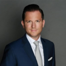 Dominique Bertolone smiling and wearing a white shirt, silver tie, and navy suit jacket