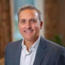 An adult with short gray hair, wearing a grey suit jacket with a white shirt.