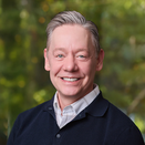 Michael Scott Smith smiling and wearing a white shirt with navy blue sweater