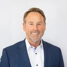 Michael Wilson smiling and wearing a white shirt with blue buttons and blue suit jacket