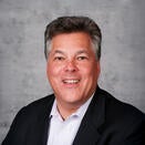 Neil Liebman smiling and wearing a white shirt with black suit jacket