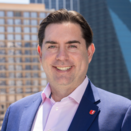 Ryan Suchala smiling and wearing a pink shirt with navy suit jacket