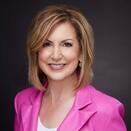 Shari Krueger smiling and wearing a white shirt and pink blazer
