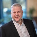 Man with grey hair and beard wearing dark jacket and white shirt