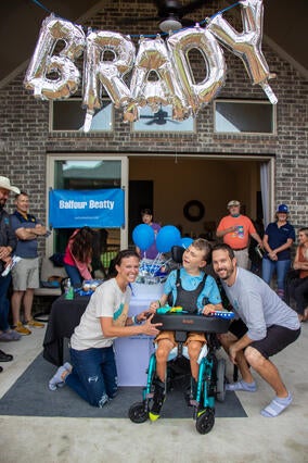 Brady and his parents smiling under balloons that say "BRADY".