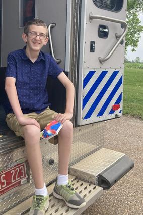 wish kid Noah perches on the back of an ambulance, and smiles at the camera