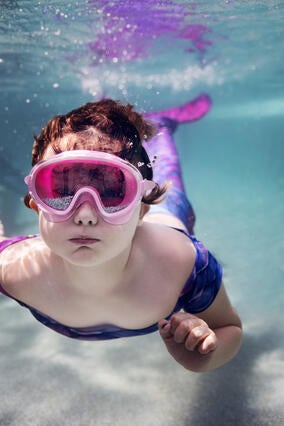 Emma underwater blowing bubbles with goggles on