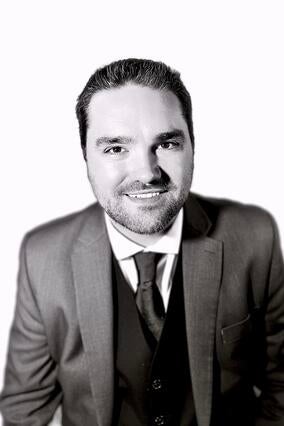 Black and white photo featuring male with gray three-piece jacket, tie and white shirt.