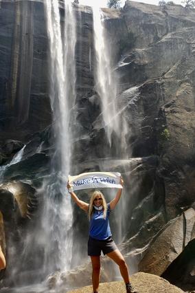 Denise holding MAW sign under a waterfall