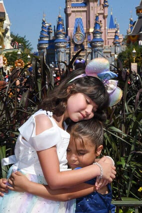 Wish kid Giselle and sister Emily hugging at Walt Disney World in front of the castle