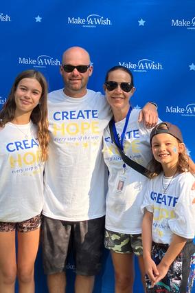 Courtney and her husband and two daughters are photographed standing in front of a Make-A-Wish step and repeat at the Walk For Wishes event.