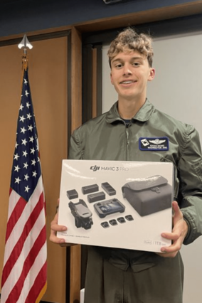 Wish kid Isaiah standing to the right of an American flag, holding a drone inside the box.