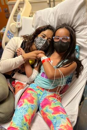Wish kid Soraya in hospital bed cuddling with mom during treatment