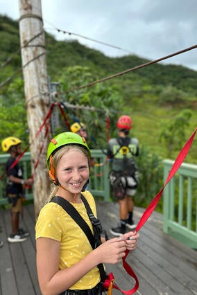 Nora wearing a helmet and protective equipment on the top of a tropical hill getting ready to zipline