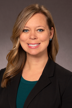 A woman in a teal blouse and black blazer smiling. 