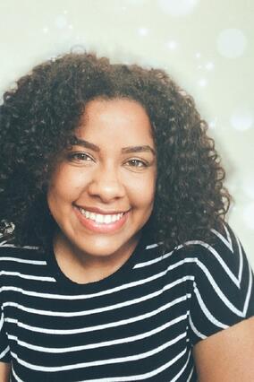 Maria smiling in front of a blank wall with a black and white striped shirt
