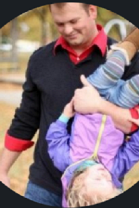 Matt in a black and red shirt holding his daughter playfully upside down at a park