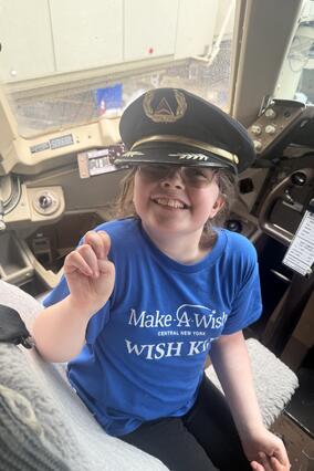 Wish kid Avery in the cockpit of a plane wearing a pilot's cap