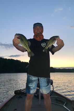 Noah holds up two fish at sunset, from the boat