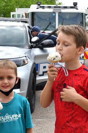 two small children hold ice cream cones with emergency vehicles in the back