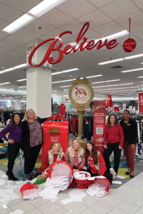 Girl Scouts, Macy's and Make-A-Wish staff pose with letters in front of Macy's Believe station at local store