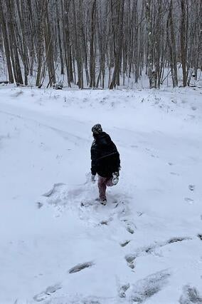 Wish kid Kayden running in the snow. He's facing away from the camera wearing a black snowsuit