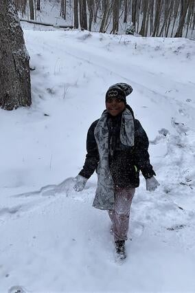 Wish kid Kayden smiling while playing in the snow. He's wearing a black snowsuit with a grey scarf.