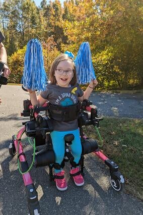 Marcy holding blue pom poms standing in her hot pink Trexo