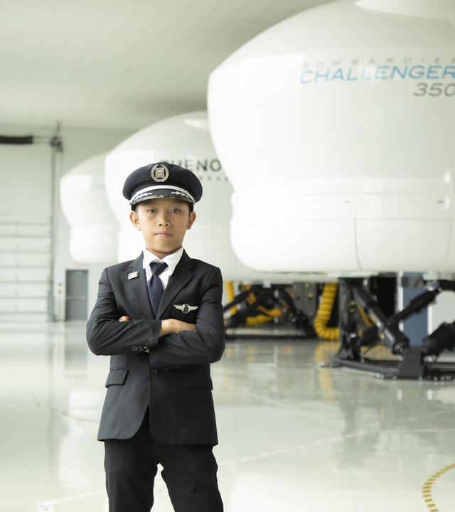 Wish kid Kael standing in an airplane hanger with his arms crossed wearing a pilot uniform