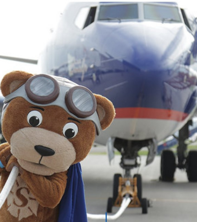 Sunny, the Sun Country Airlines mascot, pulling a plane with a rope.