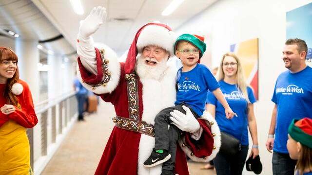 Wish kid Brantley smiling while Santa is waving and holding him.