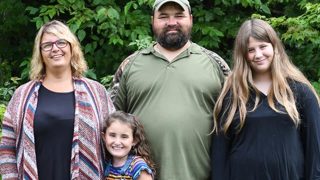 A family of four poses in front of a green background