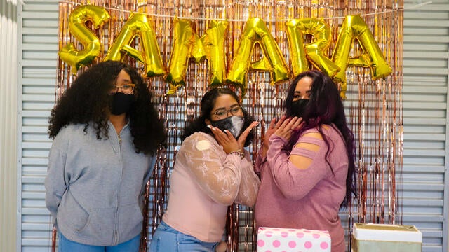Wish kid Samara posing with her sister and mom in front of her balloon sign.