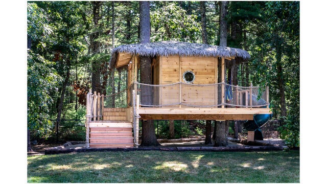 Libby's wooden treehouse nestled among the trees, with stairs and a thatched roof and a green twisty slide