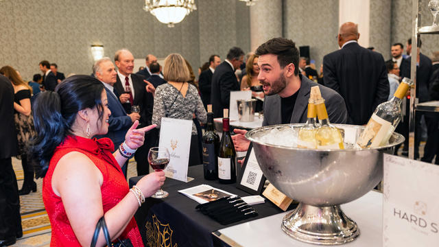 A guest in a red dress receives a glass of red wine from the wine station