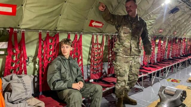 Isaiah sitting along the wall of a plane next to an instructor who is in military uniform