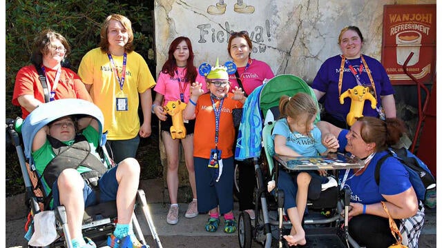 Poseidon seated front right posing with his family all wearing custom Make-A-Wish shirts in assorted colors