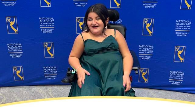 A photo of wish kid Addie in fancy dress smiling in front of a backdrop at an awards gala.