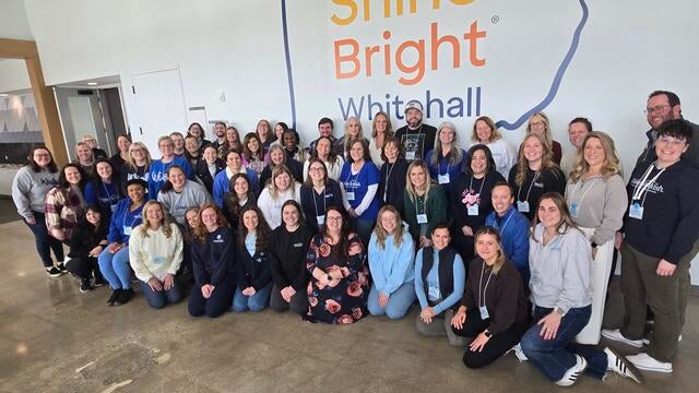 OKI staff gathers in front of the Discover Shine Bright Center logo at the All Stuff Summit