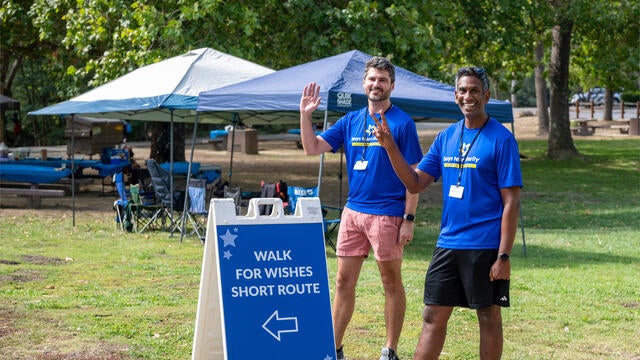 Two course monitor volunteers wave next to a wayfinding sign