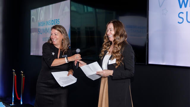 Make-A-Wish Greater Bay Area CEO Betsy Biern handing the microphone off to wish Ambassador Heather Hooper to share her story